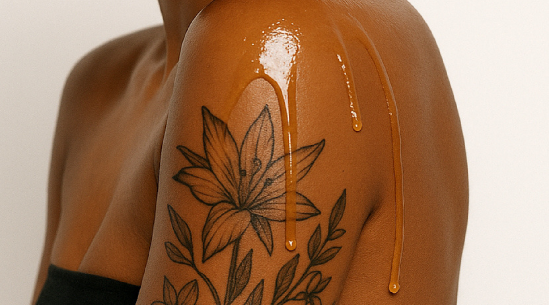 darker skin female with botanical tattoo and body oil dripping down shoulder for a blog about plant-based skincare