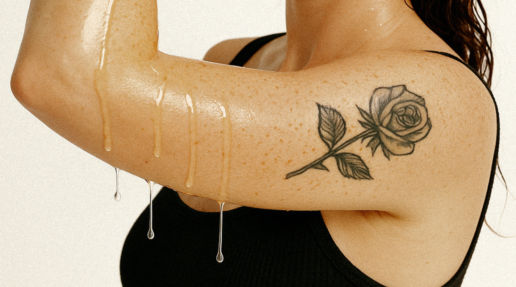 womans arm with rose tattoo and body oil dripping for a blog about body oil ingredients