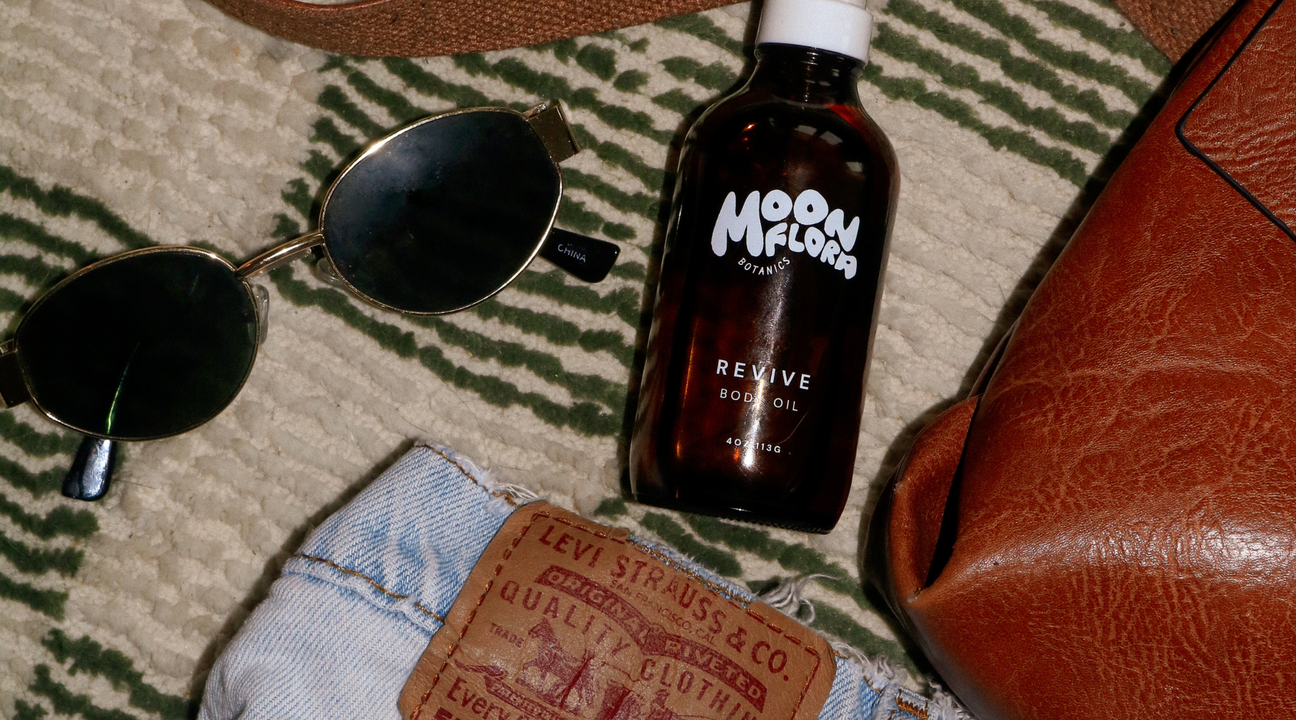 photo of moonflora revive body oil next to purse, clothes, and sunglasses for a blog discussing holiday gift basket ideas
