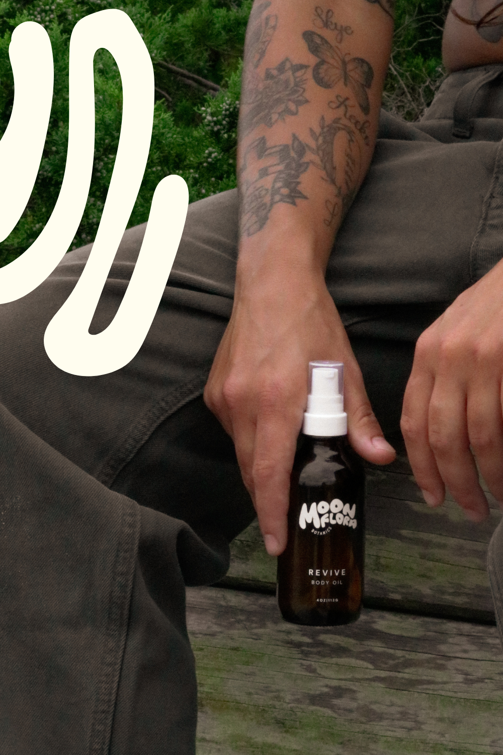 Person with tattoos holding moonflora revive body oil for a faq page about how to use body oil