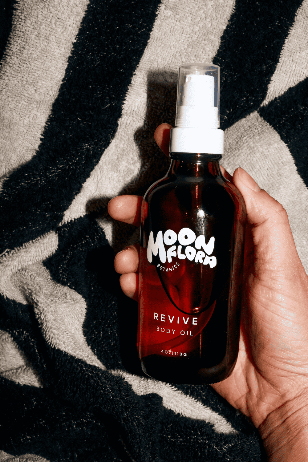 Hand holding a moonflora product bottle against a patterned fabric background