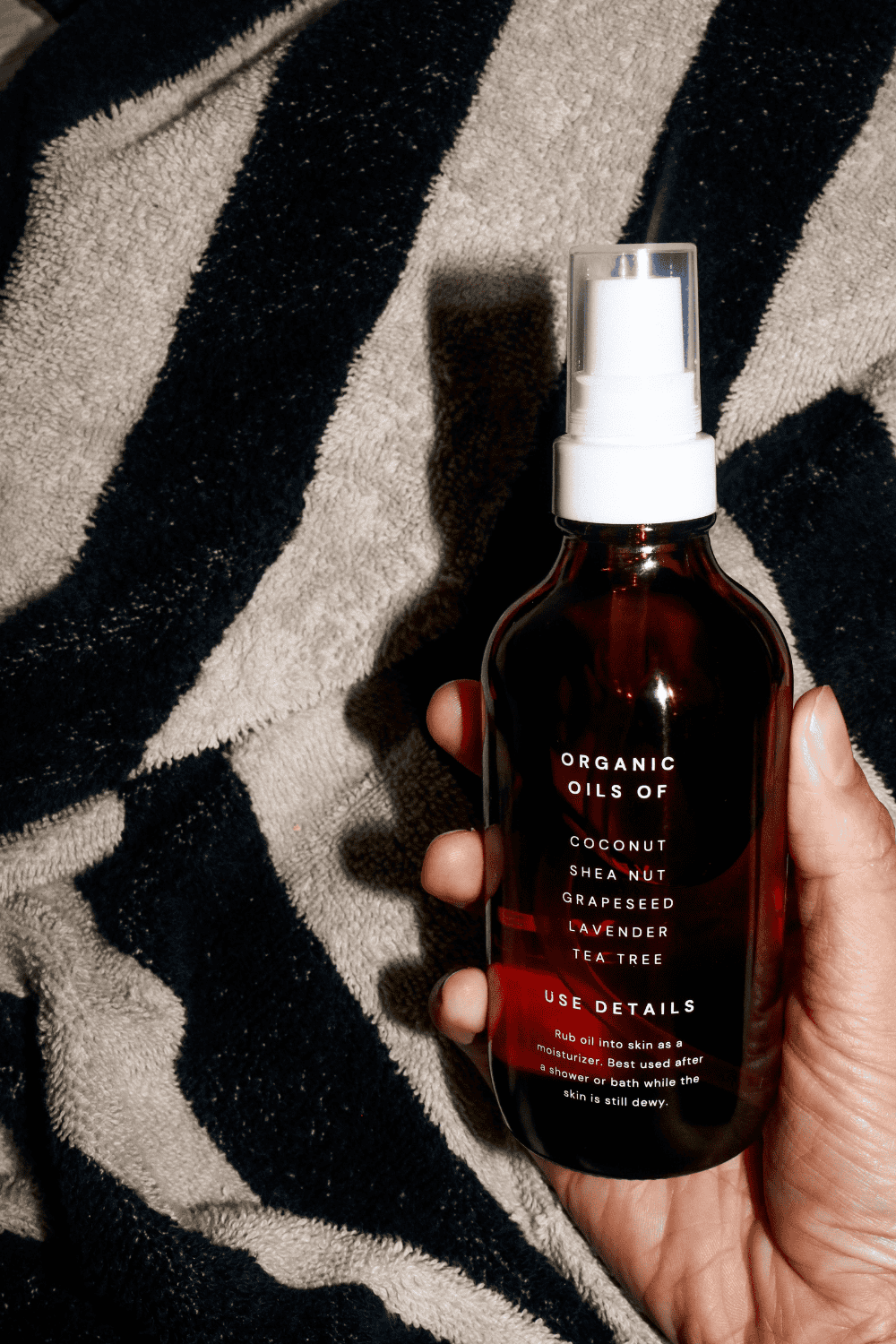 hand holding organic body oil with black and white striped background