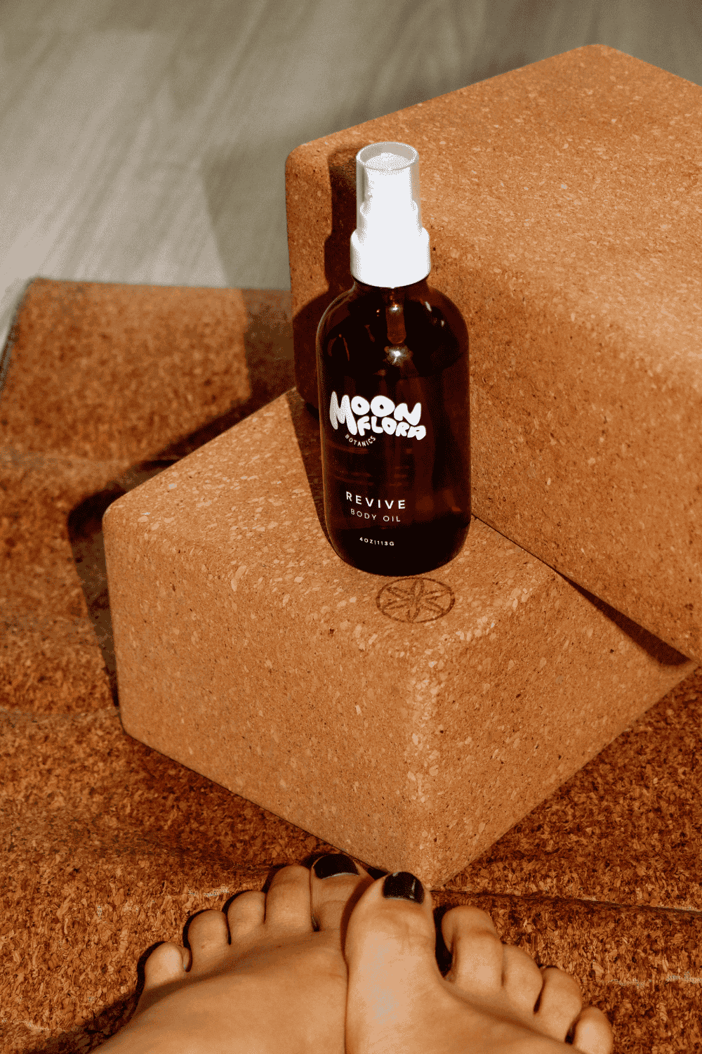 Bottle of moonflora botanics revive body oil on cork yoga blocks and mat